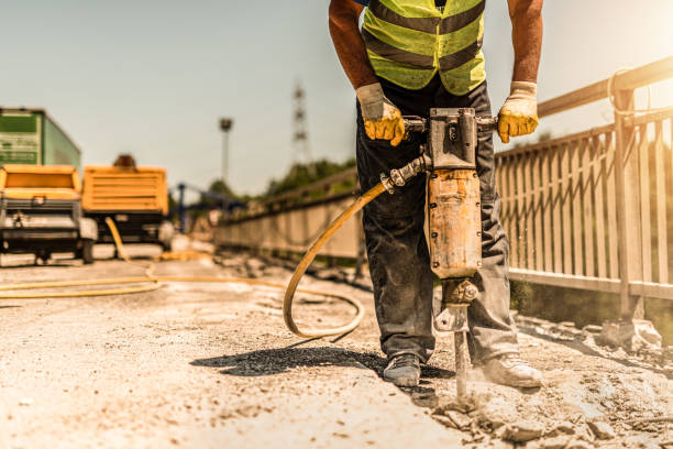 Unrecognizable manual worker using pneumatic hammer drill and repairing bridge.